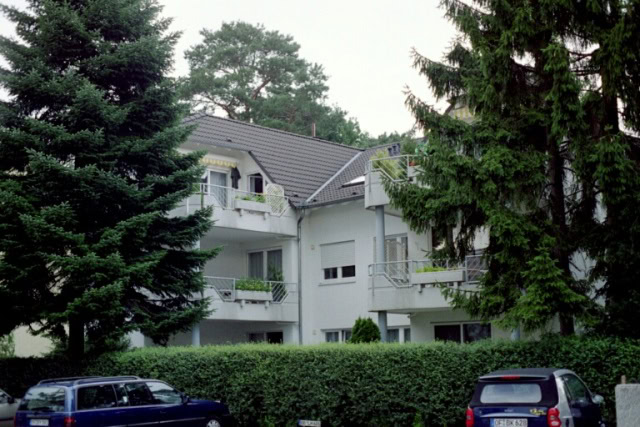 Wohnhaus mit Balkonen und Bäumen im Vordergrund.