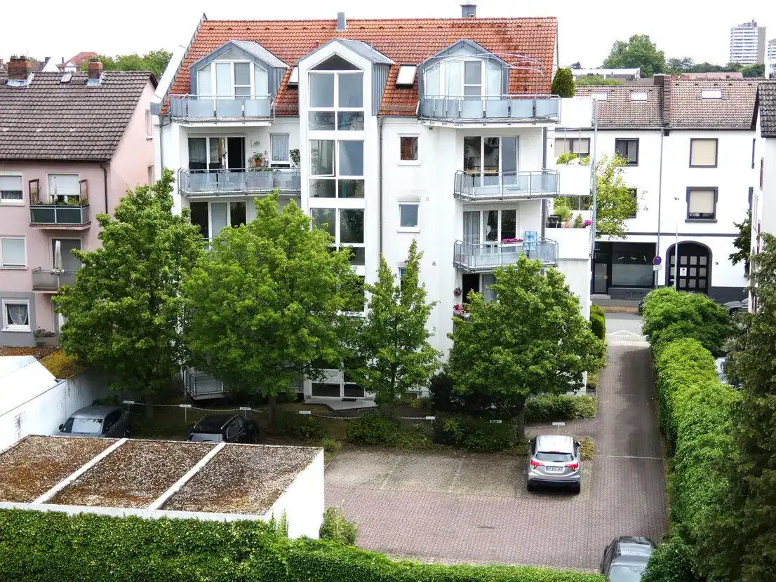 Mehrfamilienhaus mit Bäumen und Parkplätzen davor.