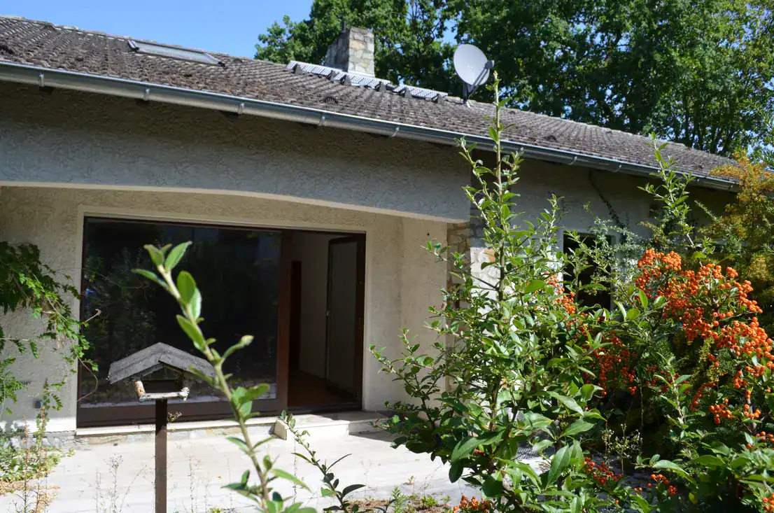 Hausfassade mit Terrasse, Gartensträuchern und Satellitenschüssel