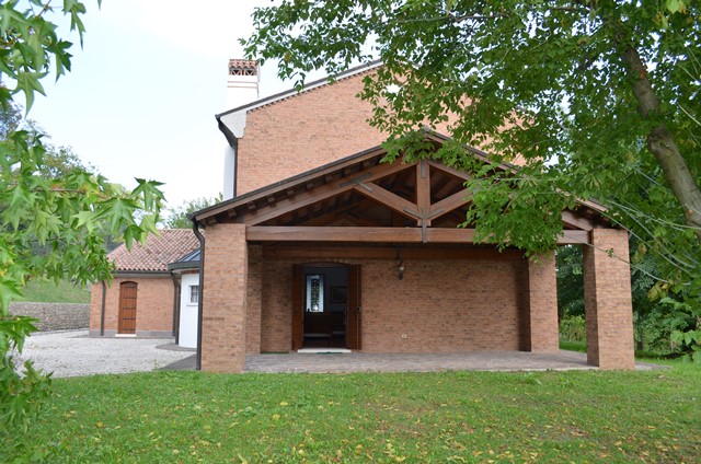 Rotes Backsteinhaus mit überdachter Veranda und grünem Garten.
