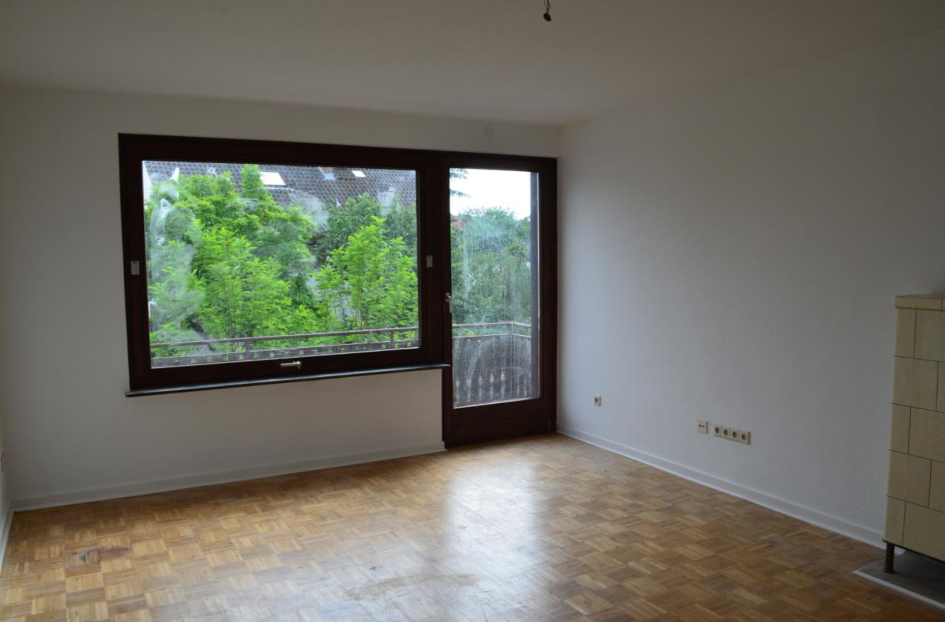 Leeres Zimmer mit großem Fenster und Parkettboden.