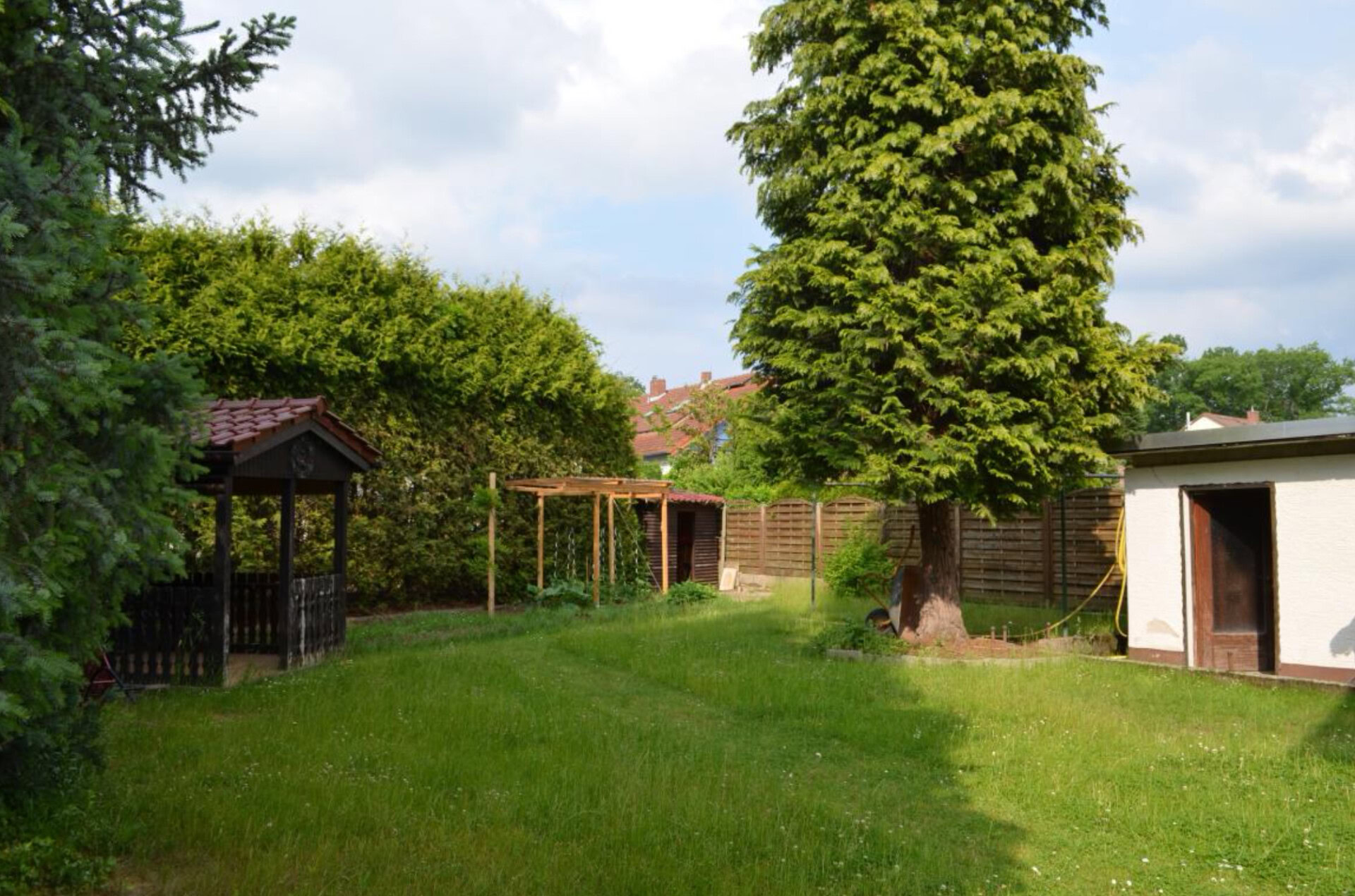 Garten mit Rasen, Bäumen und Holzhütten.