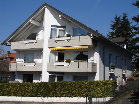 Dreistöckiges Wohnhaus mit Balkonen und Hecken