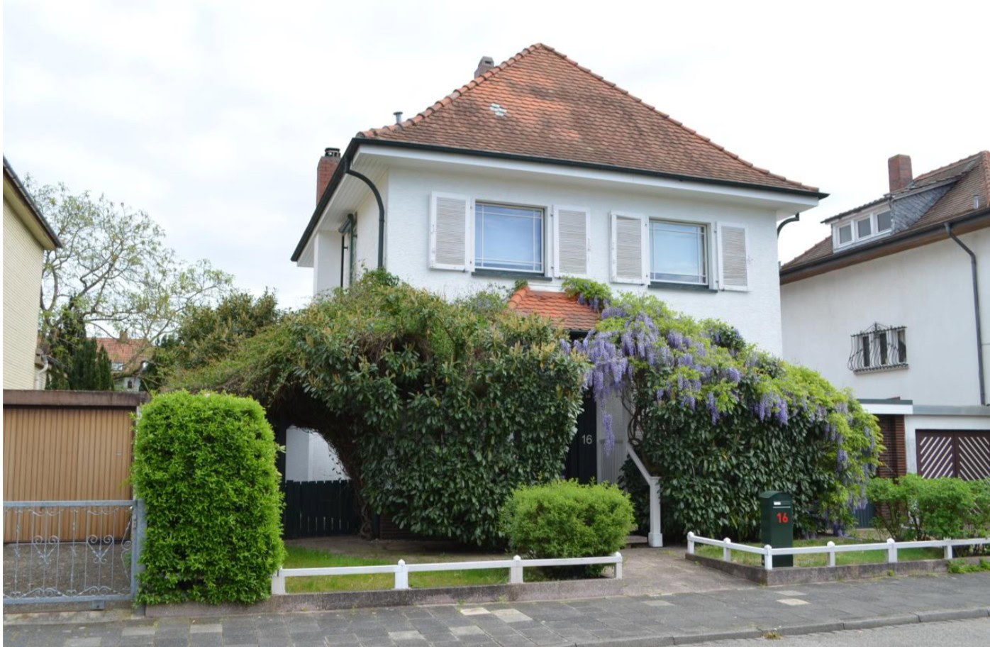 Haus mit blauer Blumenranken und grüner Umgebung.