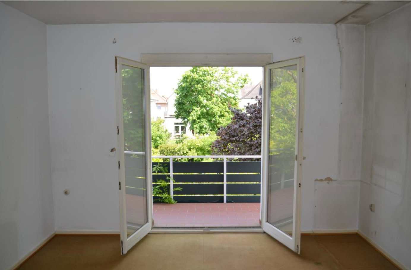 Leeres Zimmer mit Blick auf Balkon und Garten.