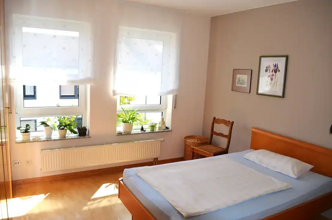Helles Schlafzimmer mit Fenster und Pflanzen.