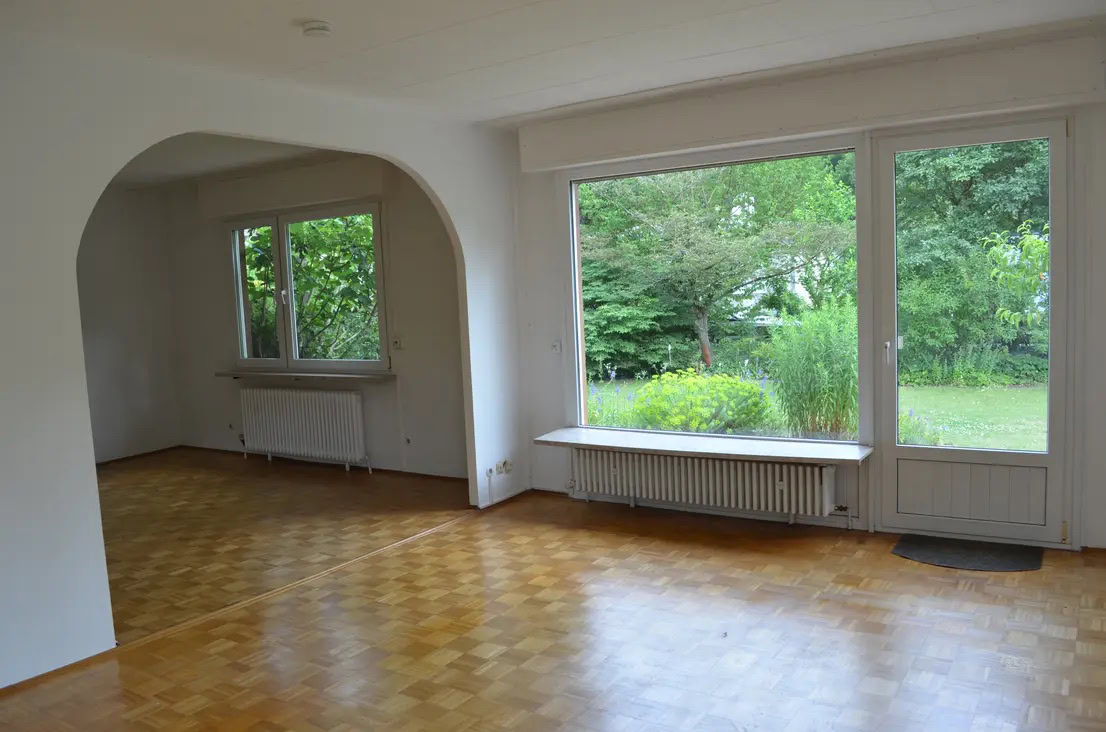 Helles Wohnzimmer mit großen Fenstern und Parkettboden.