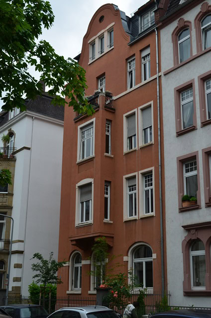 Mehrstöckiges Wohnhaus in städtischer Umgebung, Bäume im Vordergrund.