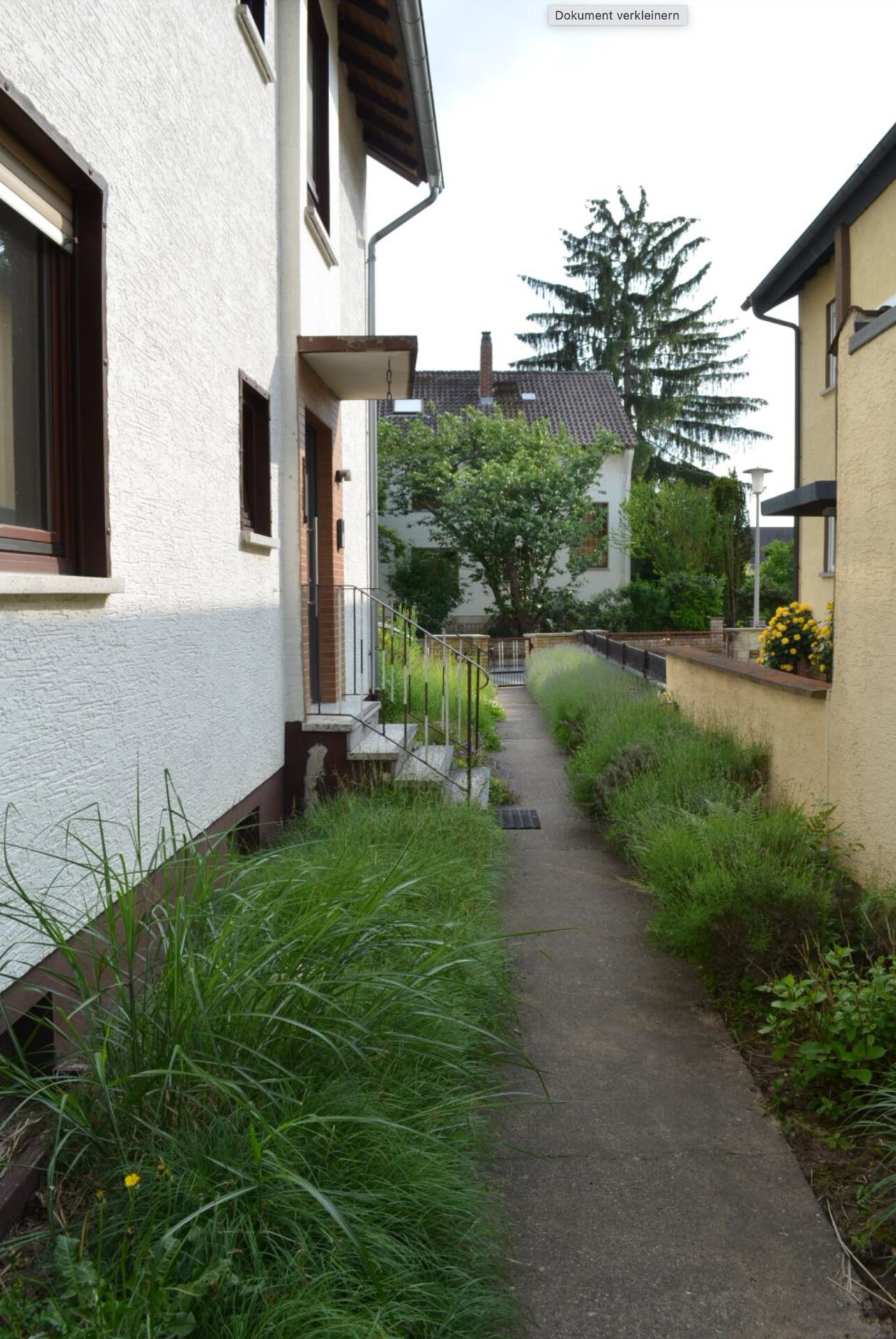 Schmaler Weg zwischen zwei Wohnhäusern mit Garten