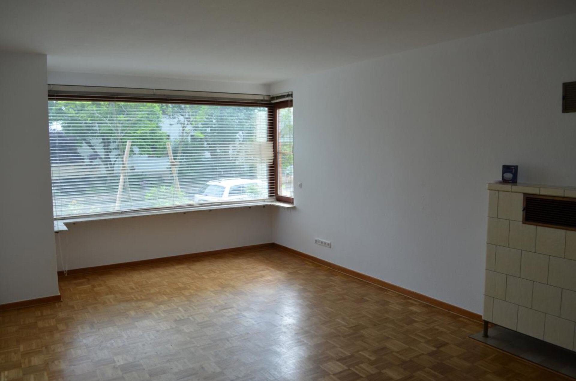 Leeres Zimmer mit großem Fenster und Parkettboden.